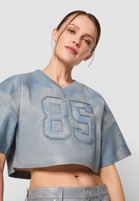 Jersey de malla azul recortado con una textura suave, que presenta un gran "85" en detalle cosido y mangas cortas.