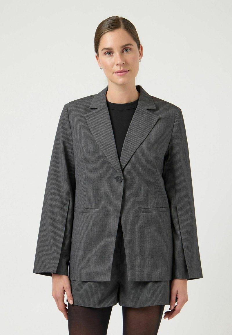 Grå stripete blazer med enkelt knappelukking, hakkede slag og forlommer, kombinert med svart topp og shorts.