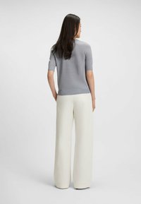 Maglietta a maniche corte grigia chiara in maglia abbinata a pantaloni bianchi a vita alta e gamba ampia; texture liscia, dettagli minimi.