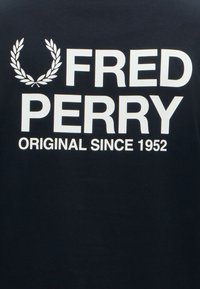 Λογότυπο Fred Perry με κείμενο και στεφάνι δάφνης σε λευκό σε μαύρο φόντο με τη φράση «Original since 1952» κάτω από το όνομα του brand.