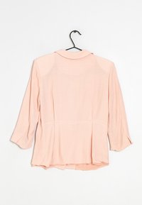 Ljusrosa, genomskinlig blus med krage, trekvartslånga ärmar och en något veckad bakdesign. Tyget ser mjukt och lätt ut.