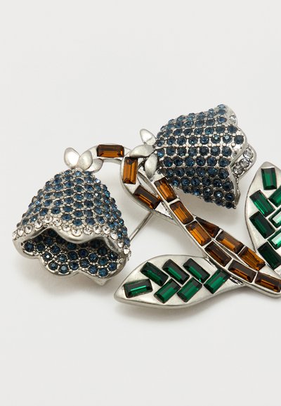 Broche florale argentée avec des fleurs en forme de cloche incrustées de pierres bleues, des pierres rectangulaires brunes sur les tiges, et des pierres rectangulaires vertes sur les feuilles.