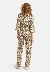 Twee-delig outfit met een beige stof en een zwart loofpatroon. Bevat driekwartmouwen en losse broek.