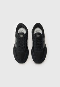 Chaussures de sport noires avec une tige en maille et en daim, bout rond, col rembourré et lacets ton sur ton. Logo visible sur le côté et sur la semelle intérieure.