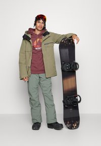 Snowboard s crnom podlogom i smešnim smešnim smešnim smešnim smešnim smešnim smešnim smešnim smešnim smešnim smešnim smešnim smešnim smešnim smešnim smešnim smešnim smešnim smešnim smešnim smešnim smešnim smešnim smešnim smešnim smešnim smešnim smešnim smešnim smešnim smešnim smešnim smešnim smešnim smešnim smešnim smešnim smešnim smešnim smešnim smešnim smešnim smešnim smešnim smešnim smešnim smešnim smešnim smešnim smešnim smešnim smešnim smešnim smešnim smešnim smešnim smešnim smešnim smešnim smešnim smešnim smešnim smešnim smešnim smešnim smešnim smešnim smešnim smešnim smešnim smešnim smešnim smešnim smešnim smešnim smešnim smešnim smešnim smešnim smešnim smešnim smešnim smešnim smešnim smešnim smešnim smešnim smešnim smešnim smešnim smešnim smešnim. Osoba nosi maslinasto zeleni kaput preko bordo dukserice i svijetlozelenih hlača.