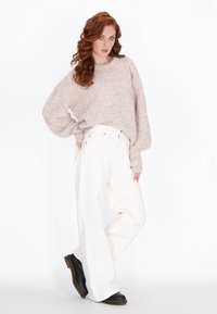 Beżowy sweter z dzianiny o luźnym kroju i szerokich rękawach, zestawiony z białymi spodniami o wysokim stanie i szerokimi nogawkami oraz czarnymi botkami za kostkę.