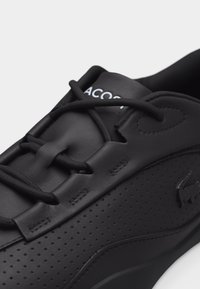 Baskets Lacoste noires en cuir perforé, avec des lacets noirs et un logo embossé sur le côté.