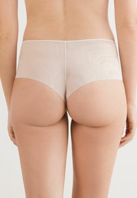 Mutande hipster beige trasparenti con una texture liscia e morbida e un design a vita bassa, caratterizzate da dettagli delle cuciture e da una forma minimalista.
