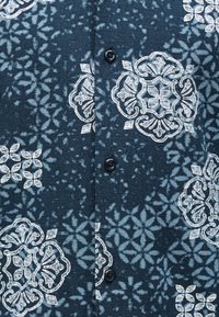 Σκούρο μπλε ύφασμα με εκλεπτυσμένα λευκά λουλουδένια και γεωμετρικά σχέδια, με τμήμα με κουμπιά σε μαύρο χρώμα.