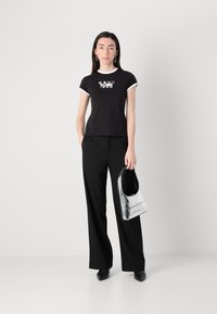 Black fitted t-shirt with white accents and graphic print, paired with black wide-leg trousers, holding a shiny silver handbag.