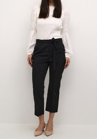 Vit, volangärmad topp med lång ärm, kombinerad med högmidjade, svarta, capribyxor med ett rosett-bälte. Skor med klack i neutral färg.