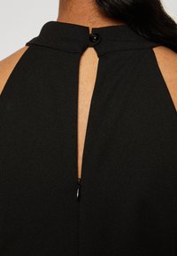Prenda negra con un cuello alto, que presenta un corte en forma de llave y una cremallera visible en la espalda. Textura suave y líneas limpias.