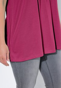 Fuksjowy, krótki top z krótkim rękawem o luźnym kroju, wykonany z miękkiego materiału, z zakończeniem sięgającym tuż nad szarymi, dopasowanymi dżinsami.