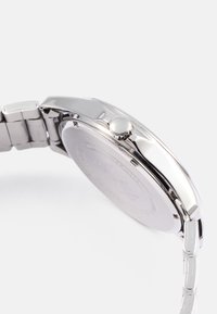 Sølv rustfrit stål ur med rund sag og poleret overflade. Har en sidekrone og et sammenkoblet armbånd med en jævn tekstur.