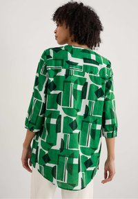 Groen patroonshirt met geometrische vormen in verschillende tinten, met driekwartmouwen en een ronde zoom. Lichtgewicht stof.