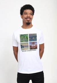 Hvid bomulds t-shirt med fire kvadratiske billeder af Monets malerier, med "OSCAR-CLAUDE MONET" trykt i sort under grafikken.