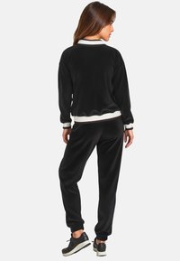 Schwarzes Fleece-Trackset mit Rundhalsausschnitt, gerippten Bündchen und Taillenbund. Die Hose hat eine schmale Passform und wird von schwarzen Sneakers ergänzt.
