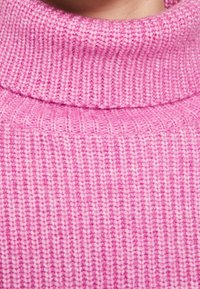 Pull roulé rose pâle en tricot avec une texture côtelée et un col épais. Gros plan sur le tissu mettant en valeur son aspect doux.