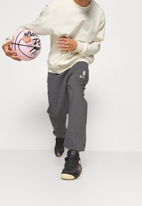 Sport outfit bestående af en lys beige sweatshirt, grå sweatpants med logo, sorte sneakers og en pink basketball med sorte markeringer.