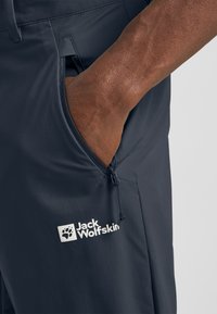 Pantaloni outdoor blu navy con una texture liscia, dotati di tasca laterale e coulisse regolabile. Presentano il logo di Jack Wolfskin in bianco.