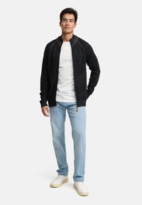Czarny kardigan na zamek z fakturowanym wykończeniem, zestawiony z białym t-shirtem, jasnoniebieskimi dżinsami i białymi trampkami. Casualowy krój o nowoczesnym designie.
