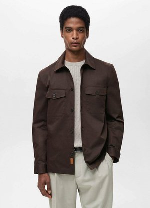 Brown button-up jacket made of cotton with two chest pockets, a collar, and a smooth texture, layered over a light sweater.