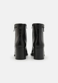 Botas de tobillo de cuero negro con una textura suave, con cierres de cremallera y un tacón de bloque apilado. Diseñadas para un ajuste ceñido.