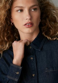 Dunkelblaue Jeanshemd mit spitzem Kragen und Knopfverschluss. Sichtbare Nähte und eine Brusttasche. Leicht strukturierter Stoff.