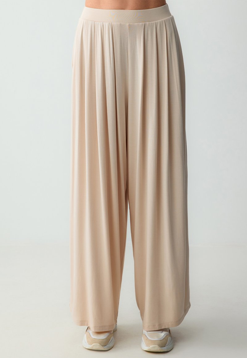 Beige wijde broek met een zachte, vloeiende textuur en een comfortabele elastische tailleband, met een losse pasvorm en subtiele draping.