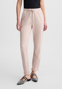 Helle rosa Jogginghosen mit einem Kordelzugbund, schmalem Schnitt und glatter Textur, kombiniert mit schwarzen Ballerinas, die mit silbernen Nieten verziert sind.