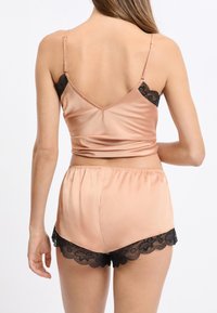 Satynowa koszulka na cienkich, regulowanych ramiączkach w odcieniu pudrowego różu, zestawiona z pasującymi szortami ozdobionymi czarną koronką na dole. Gładka faktura.