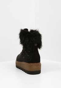 Botín negro hasta el tobillo con un collar esponjoso, tejido texturizado, suela gruesa y cordones decorativos, presentado sobre un fondo liso.