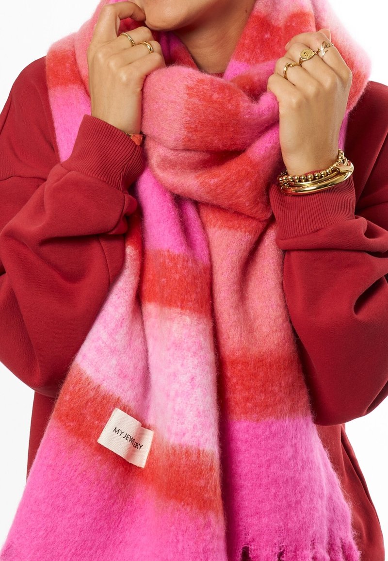 Scarf a strisce rosa e rosse realizzata in materiale morbido e peloso, con un'etichetta con scritto "MYJEWELRY" e bordi frangiati per un ulteriore effetto tattile.