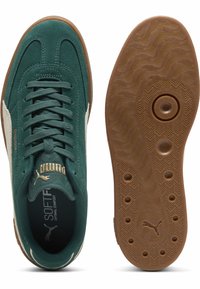 Baskets en daim vert avec semelle en caoutchouc, bande blanche sur le côté, lacet à l'avant et logo Puma doré sur la languette. La texture est lisse et durable.