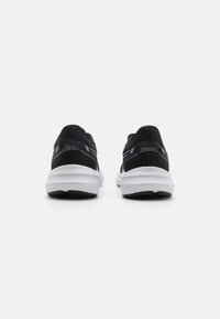 Baskets de sport noires avec une tige en mesh, semelle blanche contrastante et accents réfléchissants sur le talon. Conçues pour le confort et le soutien.