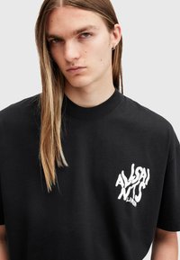 Camiseta de algodón negra con un logotipo distorsionado en blanco en el lado izquierdo del pecho, corte clásico y cuello redondo. Textura suave, manga corta.