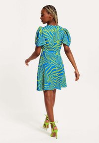 Short-sleeved dress in blue with green zebra stripes, fitted waist, flared skirt, paired with vibrant green stiletto heels.