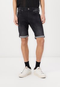Dark denim shorts with rolled cuffs, five-pocket design, and a button closure. Worn with white sneakers and black socks, on a neutral background.