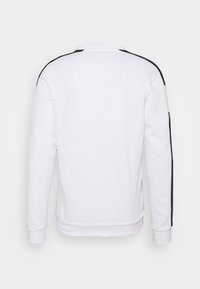 Sweat-shirt blanc à manches longues, col rond, avec des rayures latérales noires. Confectionné dans un tissu doux à texture lisse avec des poignets côtelés.