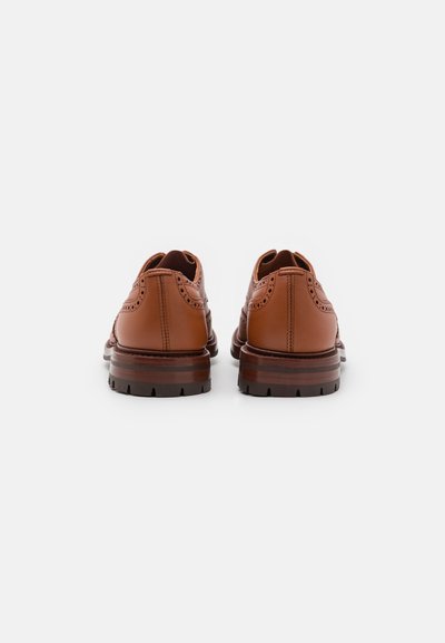 Zapatos de cuero marrón con detalles de brogue, puntera redondeada y suela de goma gruesa. Acabado suave con tacón apilado.