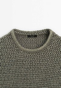 Gros plan d'un pull tricoté gris et noir avec un col rond et une petite étiquette de marque noire à l'intérieur du col.