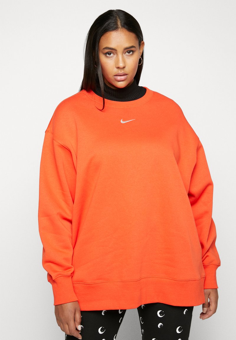 Sweatshirt surdimensionné orange avec un col rond et des accents côtelés ; présente un petit logo Nike blanc sur la poitrine. Accompagné de leggings à motifs.