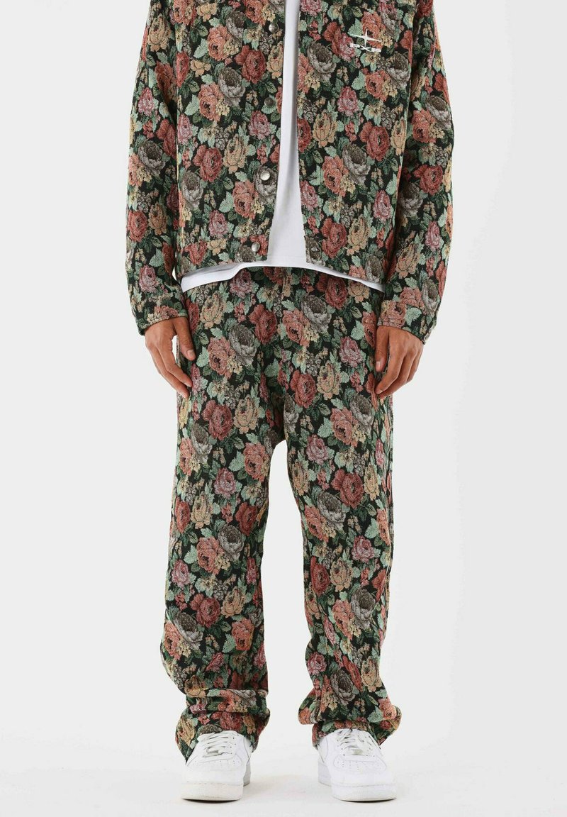Conjunto de chaqueta y pantalones de mezclilla con estampado floral, que presenta un fondo negro con diseños de rosas en color rosa, rojo y verde. Zapatillas blancas completan el look.