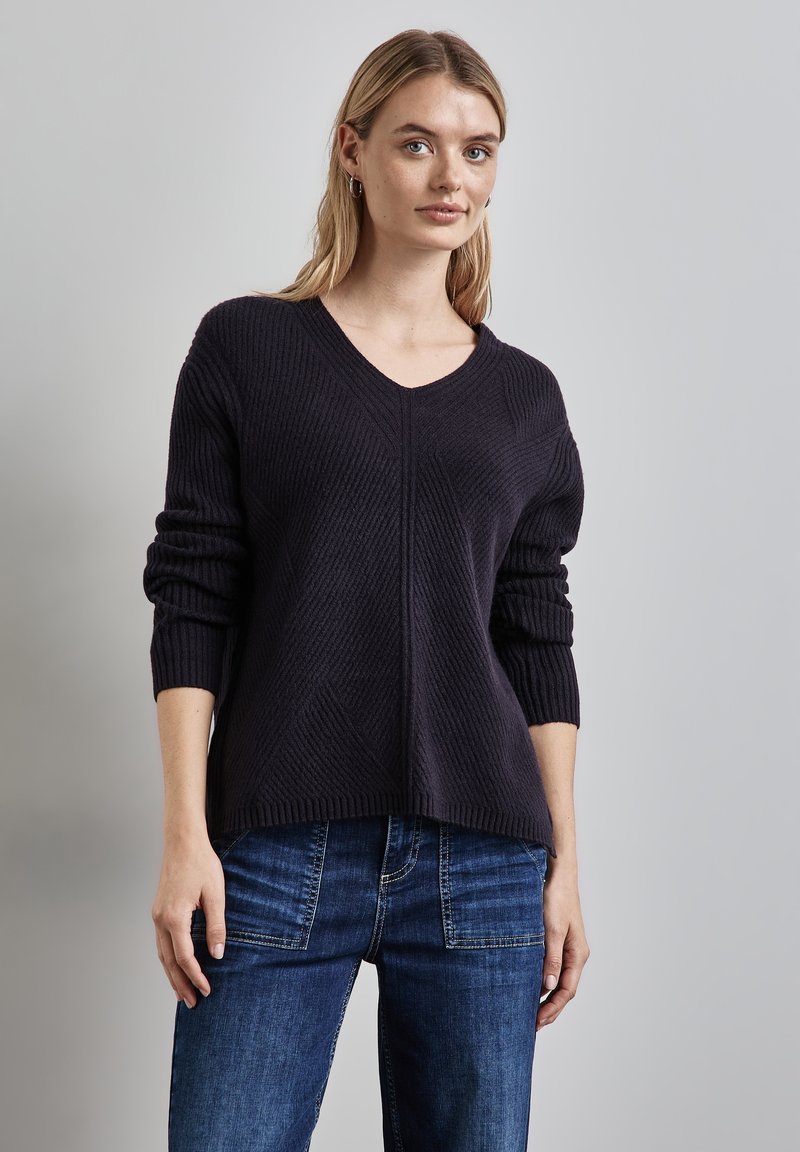 Dunkelblaues, gestricktes Sweatshirt mit V-Ausschnitt, gerippter Textur, überschnittenen Schultern und einer lockeren Passform, kombiniert mit blauen Jeans.