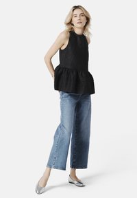 Černý bezrukávový peplum top s texturovaným materiálem, kombinovaný se světle modrými širokými džínami a stříbrnými balerínami.