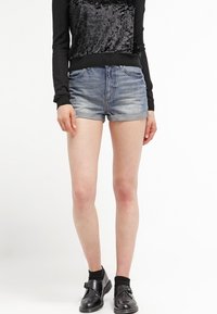 Džínové šortky ve vybledlé modré barvě s ohrnutým lemem, spárované s černým topem s dlouhým rukávem, který má na přední straně sametový panel.