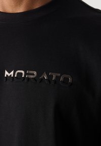 Tricou negru din bumbac, cu un logo texturat și metalizat "MORATO" pe piept. Design cu guler rotund și mâneci scurte.