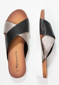 Schwarze und metallic-silberne Sandalen mit Kreuzriemen, einem strukturierten Obermaterial, braunem Fußbett und einer weißen, geriffelten Außensohle. Markenname "Tamaris" innen aufgedruckt.