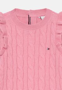 Pullover rosa lavorato a maglia con motivo a treccia, scollo a coste e maniche arricciate. Piccolo logo del brand sul lato sinistro. Tessuto morbido.