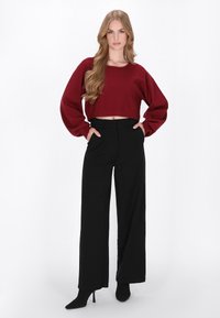 Bordeaux cropped sweater met lange mouwen, gecombineerd met zwarte wijde broek. Het model draagt ook zwarte puntige hakken. Eenvoudig, strak ontwerp.